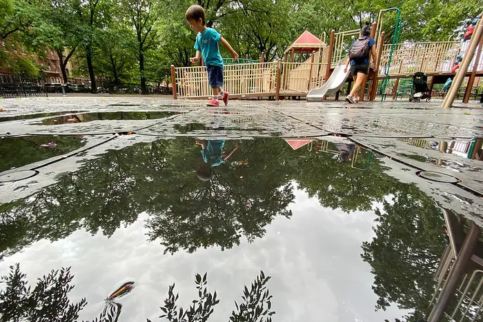 A kid walks by a puddle in a NYC playground.